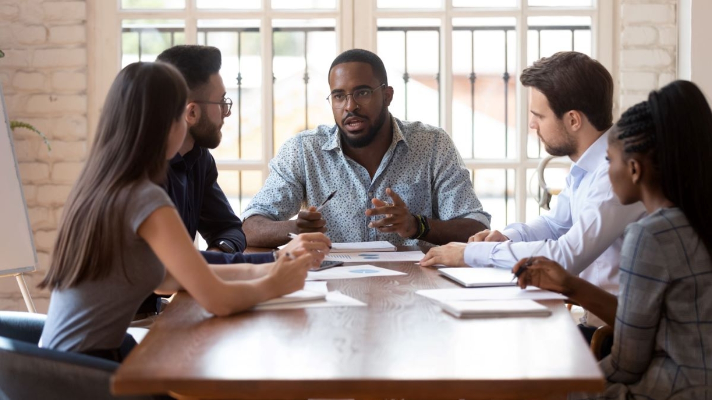 Office colleagues engaged in a productive and cheerful group meeting, with one team member presenting something on a tablet.