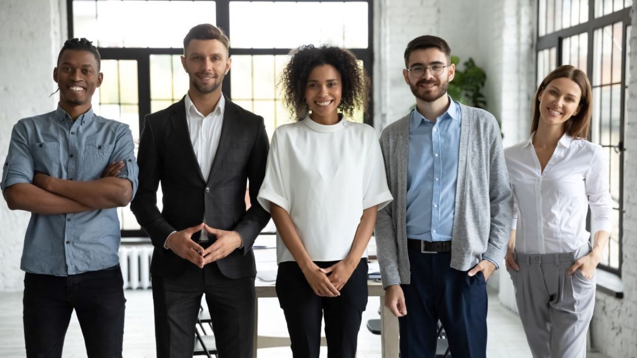 Office environment with five coworkers smiling and standing