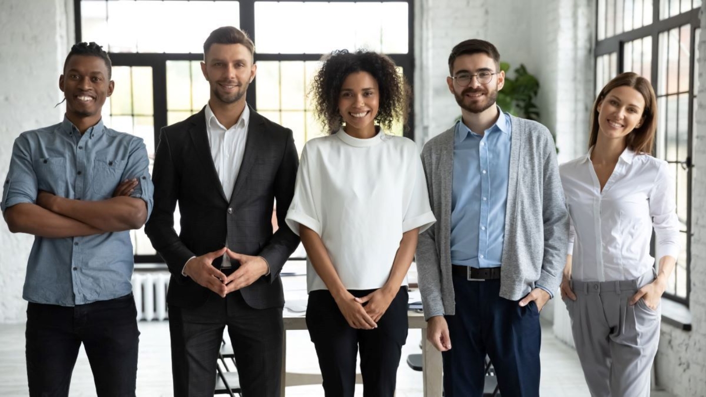Office environment with five coworkers smiling and standing