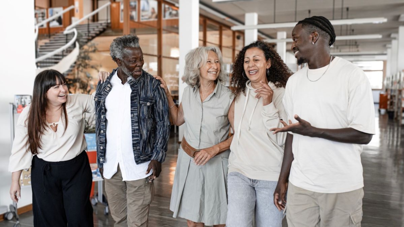 A group of five diverse people, smiling and walking together through a bright, modern office space.