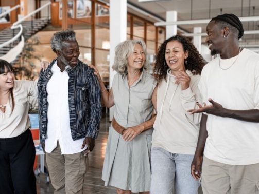 A group of five diverse people, smiling and walking together through a bright, modern office space.